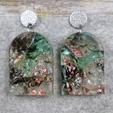 A pair of one of a kind arch shaped recycled acrylic earrings with green and pink design titled 'Enchanted Forest' and stainless steel toppers. Pair 103-07