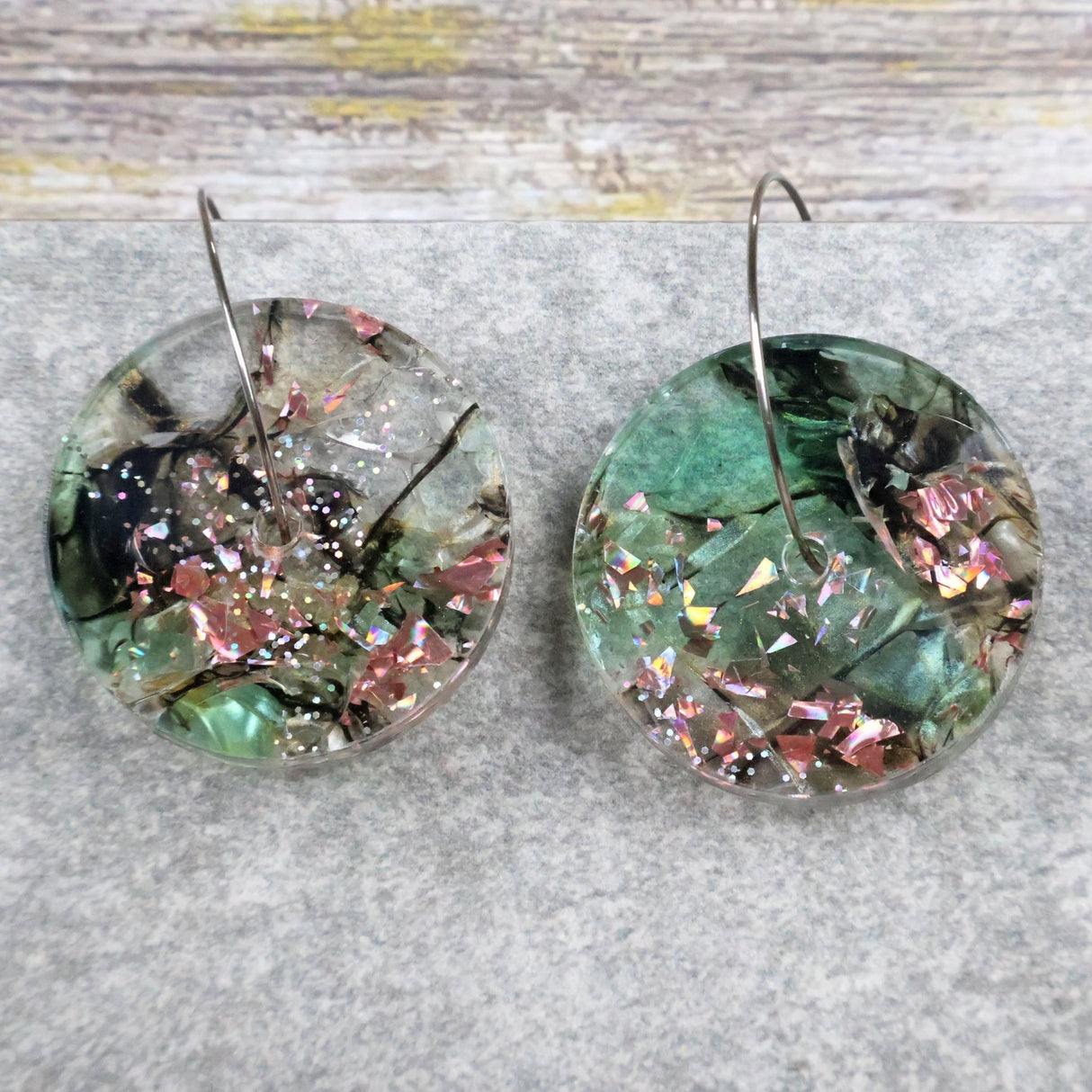 A pair of one of a kind disc shaped recycled acrylic earrings on stainless steel hoops with green and pink acrylics titled 'Enchanted Forest'. Pair 03-12