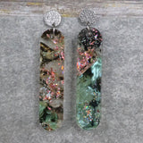 A pair of one of a kind long oval shaped recycled acrylic earrings with green and pink design titled 'Enchanted Forest' and stainless steel toppers. Pair 103-13