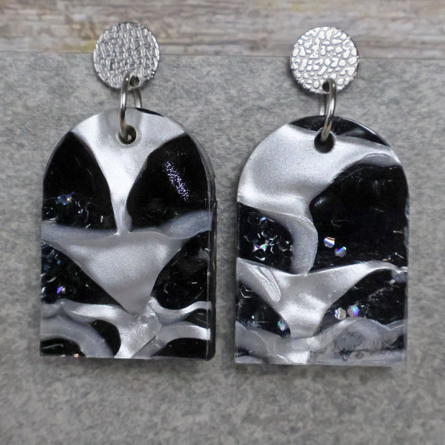 A pair of one of a kind arch shaped recycled acrylic earrings with black and white design titled 'Lunar Edge' and stainless steel toppers. Pair 104-02