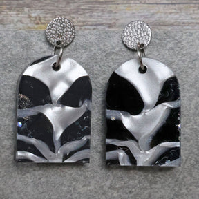 A pair of one of a kind arch shaped recycled acrylic earrings with black and white design titled 'Lunar Edge' and stainless steel toppers. Pair 104-04