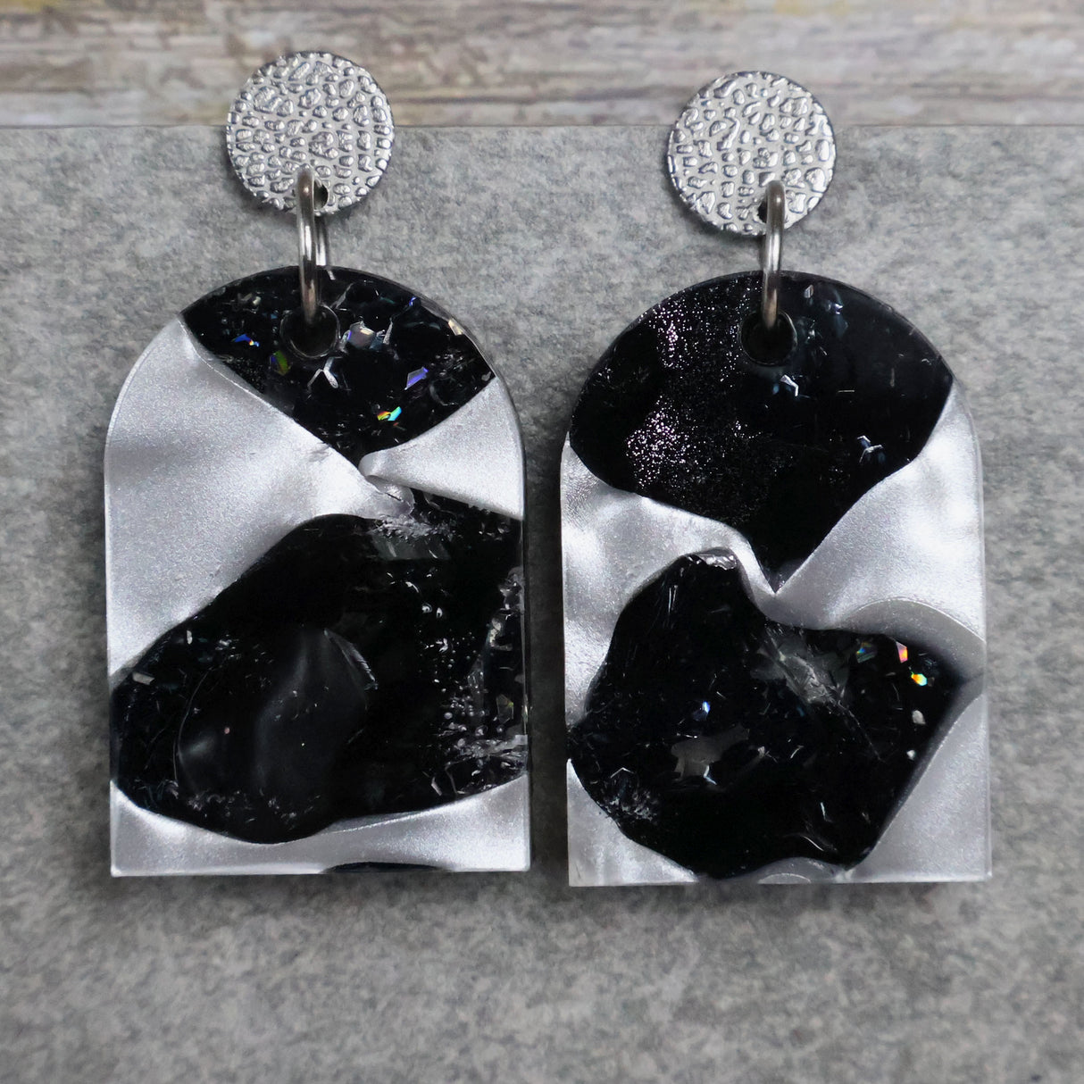 A pair of one of a kind arch shaped recycled acrylic earrings with black and white design titled 'Lunar Edge' and stainless steel toppers. Pair 104-06