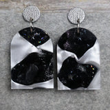 A pair of one of a kind arch shaped recycled acrylic earrings with black and white design titled 'Lunar Edge' and stainless steel toppers. Pair 104-06