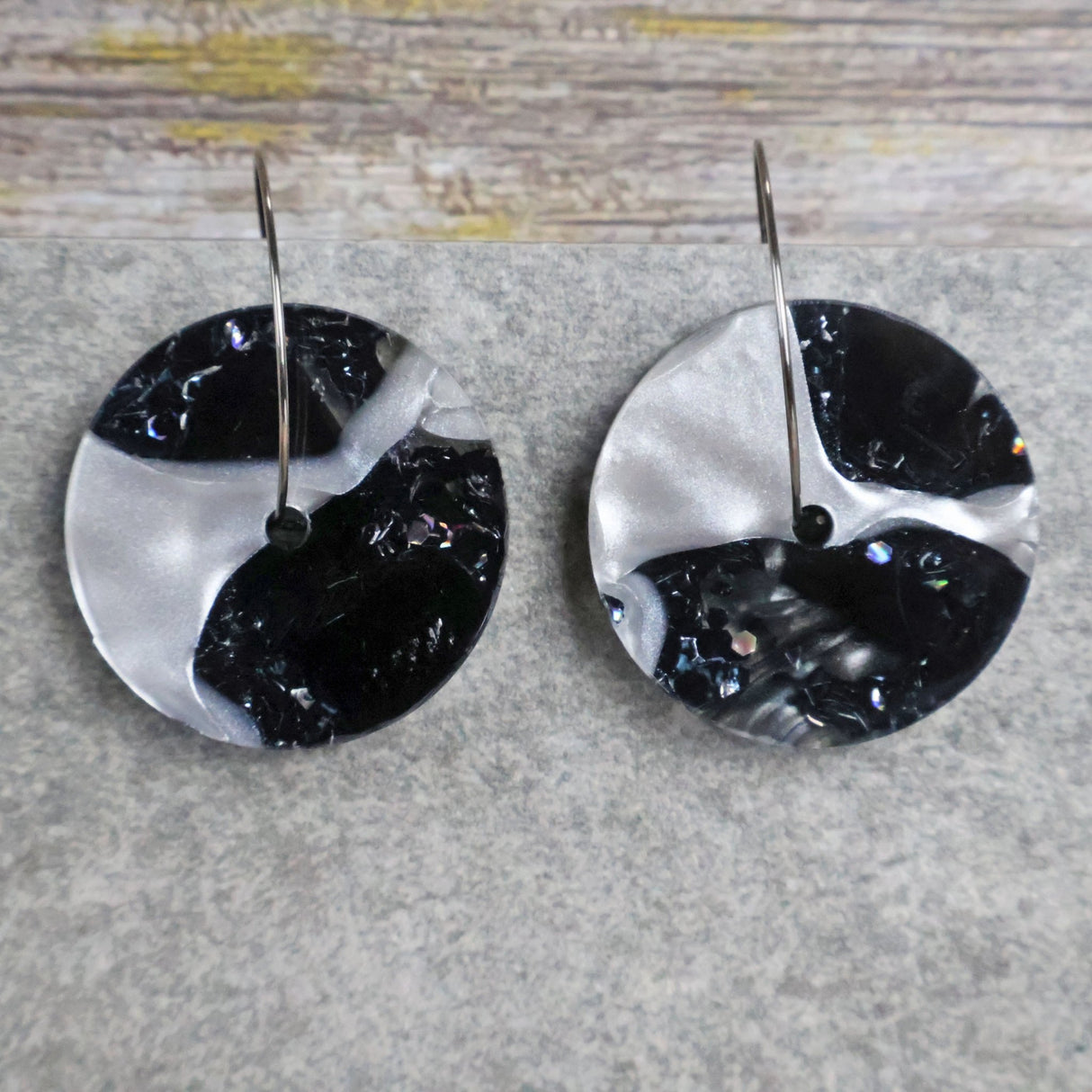 A pair of one of a kind arch shaped recycled acrylic earrings with black and white design titled 'Lunar Edge' and stainless steel toppers. Pair 104-08