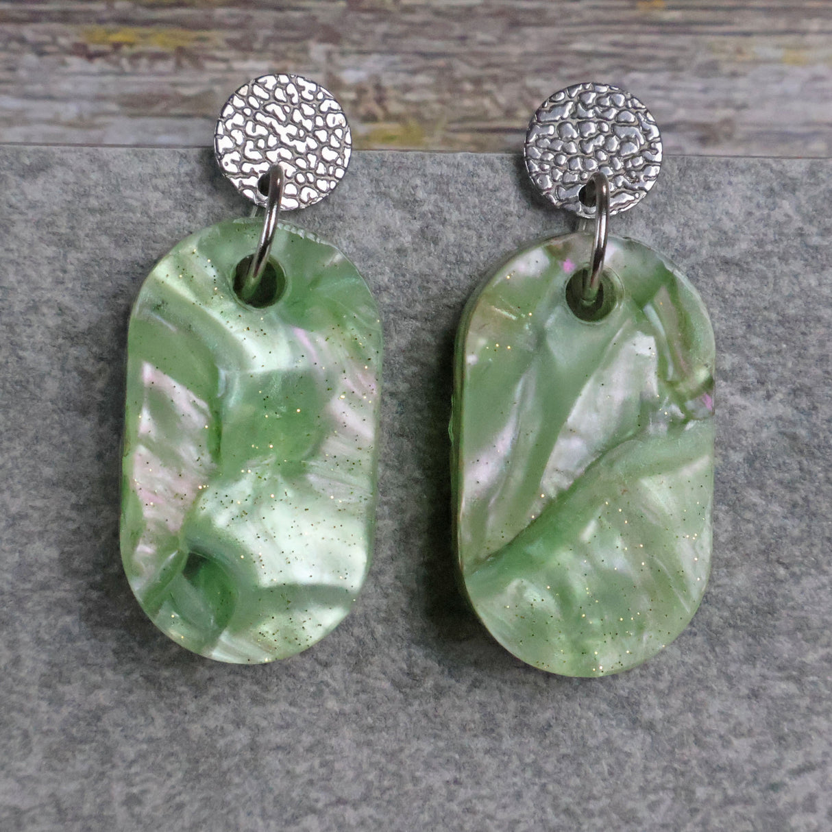 Pair of one of a kind small oval shaped recycled acrylic earrings featuring green acrylics and stainless steel toppers. Pair 105-04