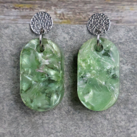Pair of one of a kind small oval shaped recycled acrylic earrings featuring green acrylics and stainless steel toppers. Pair 105-05