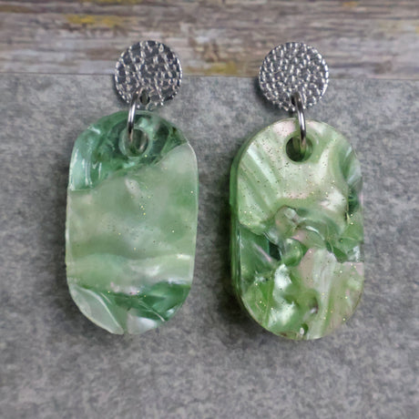 Pair of one of a kind small oval shaped recycled acrylic earrings featuring green acrylics and stainless steel toppers. Pair 105-06