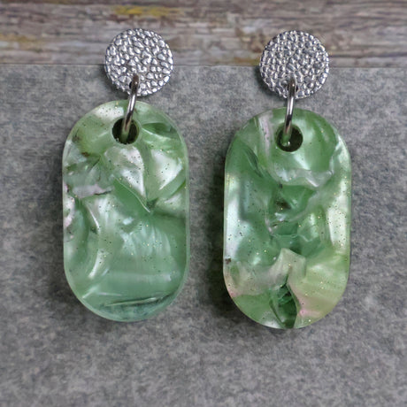 Pair of one of a kind small oval shaped recycled acrylic earrings featuring green acrylics and stainless steel toppers. Pair 105-07