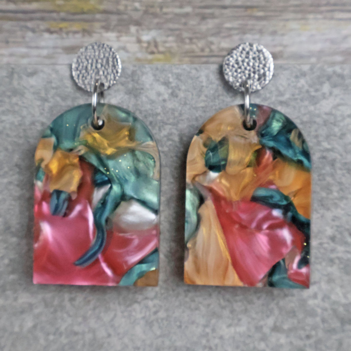 Pair of one of a kind arch shaped acrylic earrings with multicolored  design titled 'Sunset Reef' and stainless steel toppers on a gray background. Pair 106-01