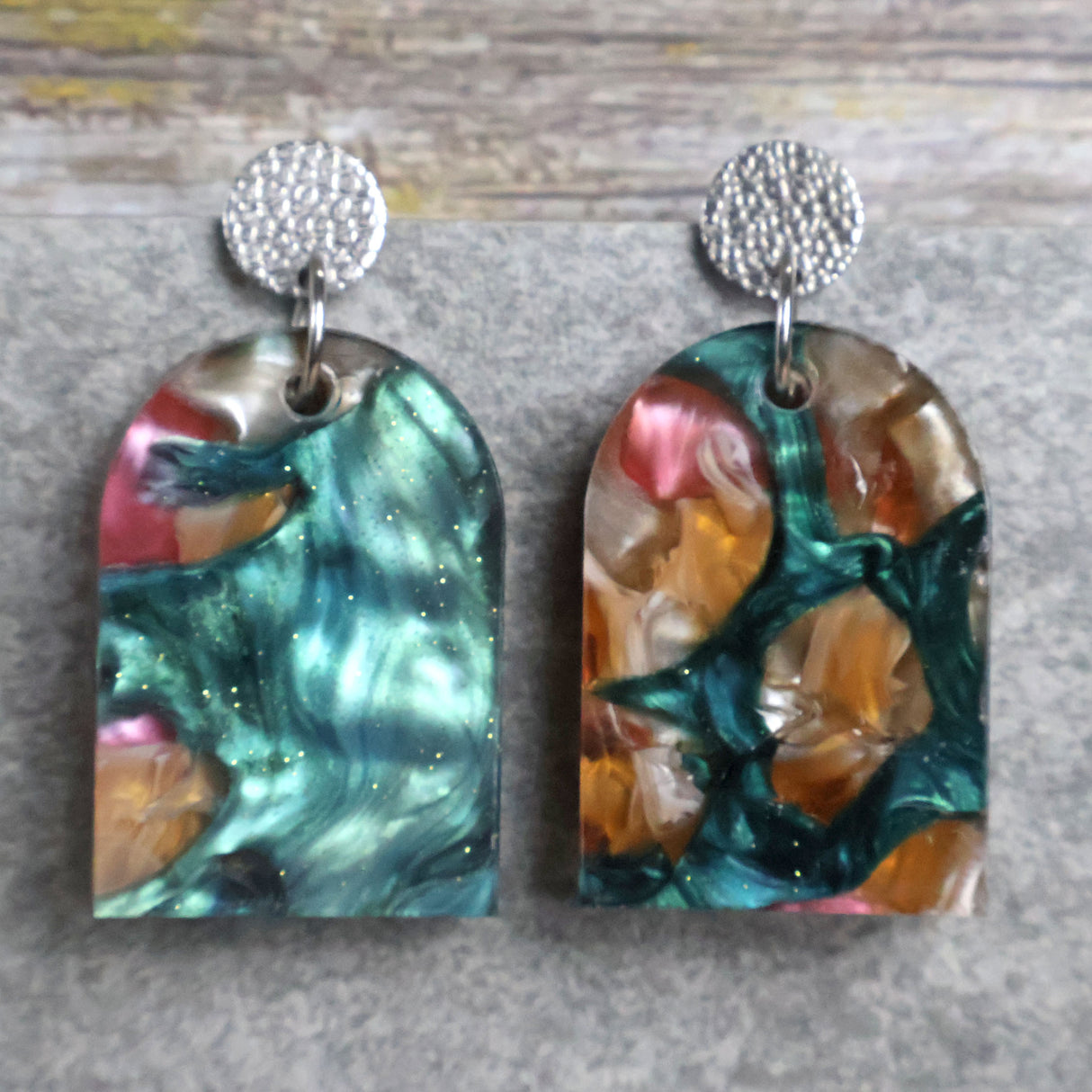 Pair of one of a kind arch shaped acrylic earrings with multicolored  design titled 'Sunset Reef' and stainless steel toppers on a gray background. Pair 106-03