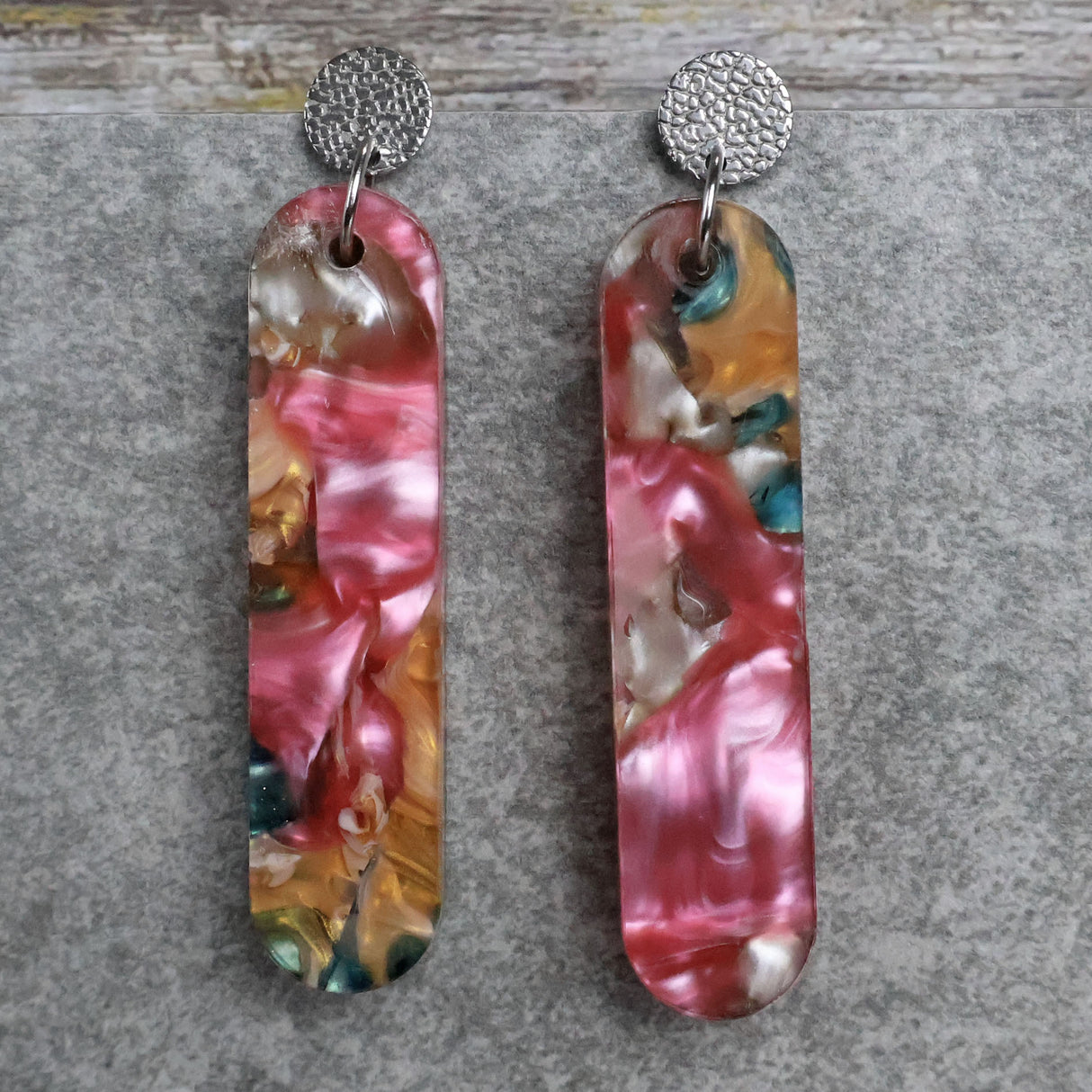 Pair of one of a kind long bar shaped acrylic earrings with multicolored  design titled 'Sunset Reef' and stainless steel toppers on a gray background. Pair 106-06
