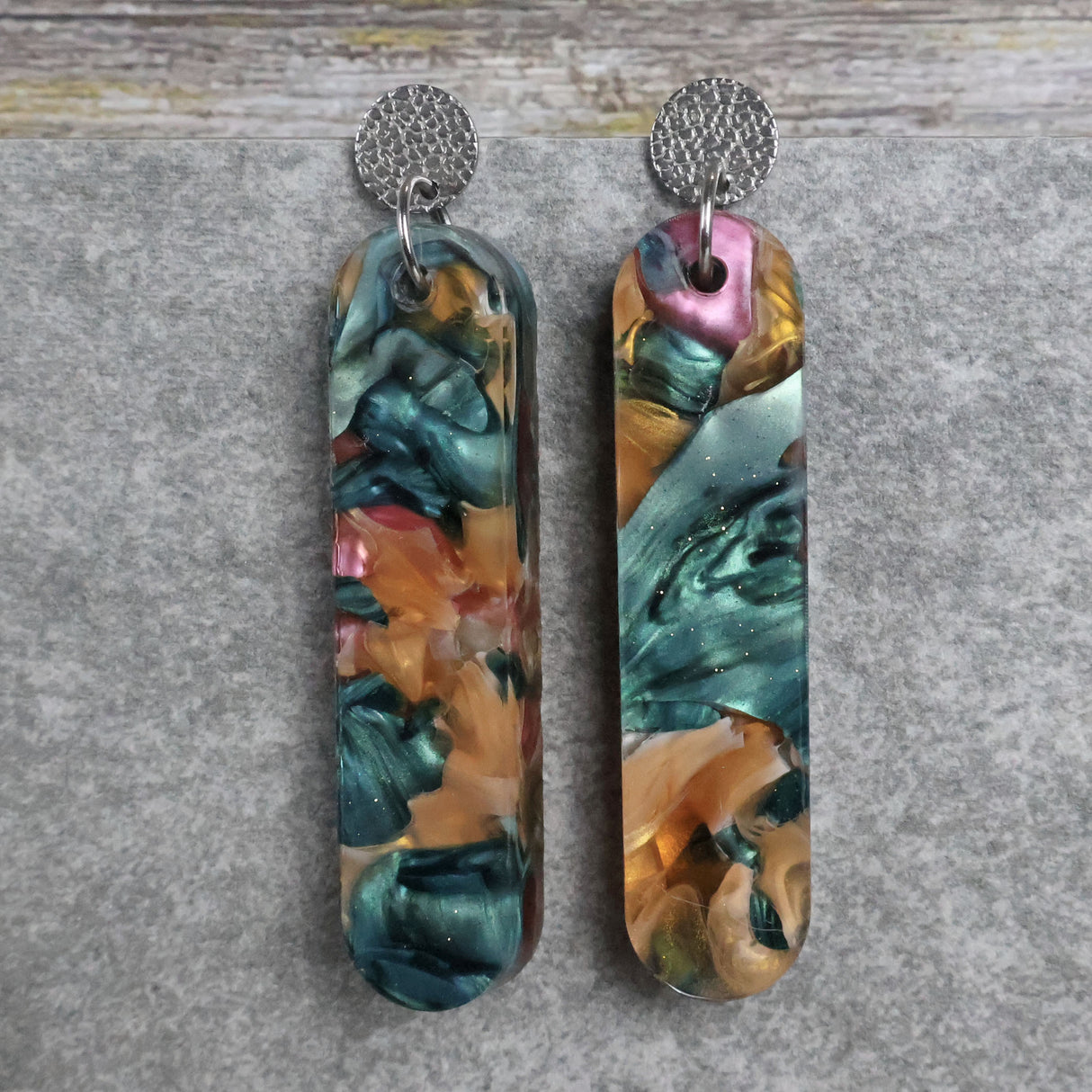 Pair of one of a kind long bar shaped acrylic earrings with multicolored  design titled 'Sunset Reef' and stainless steel toppers on a gray background. Pair 106-08