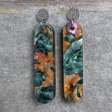 Pair of one of a kind long bar shaped acrylic earrings with multicolored  design titled 'Sunset Reef' and stainless steel toppers on a gray background. Pair 106-08