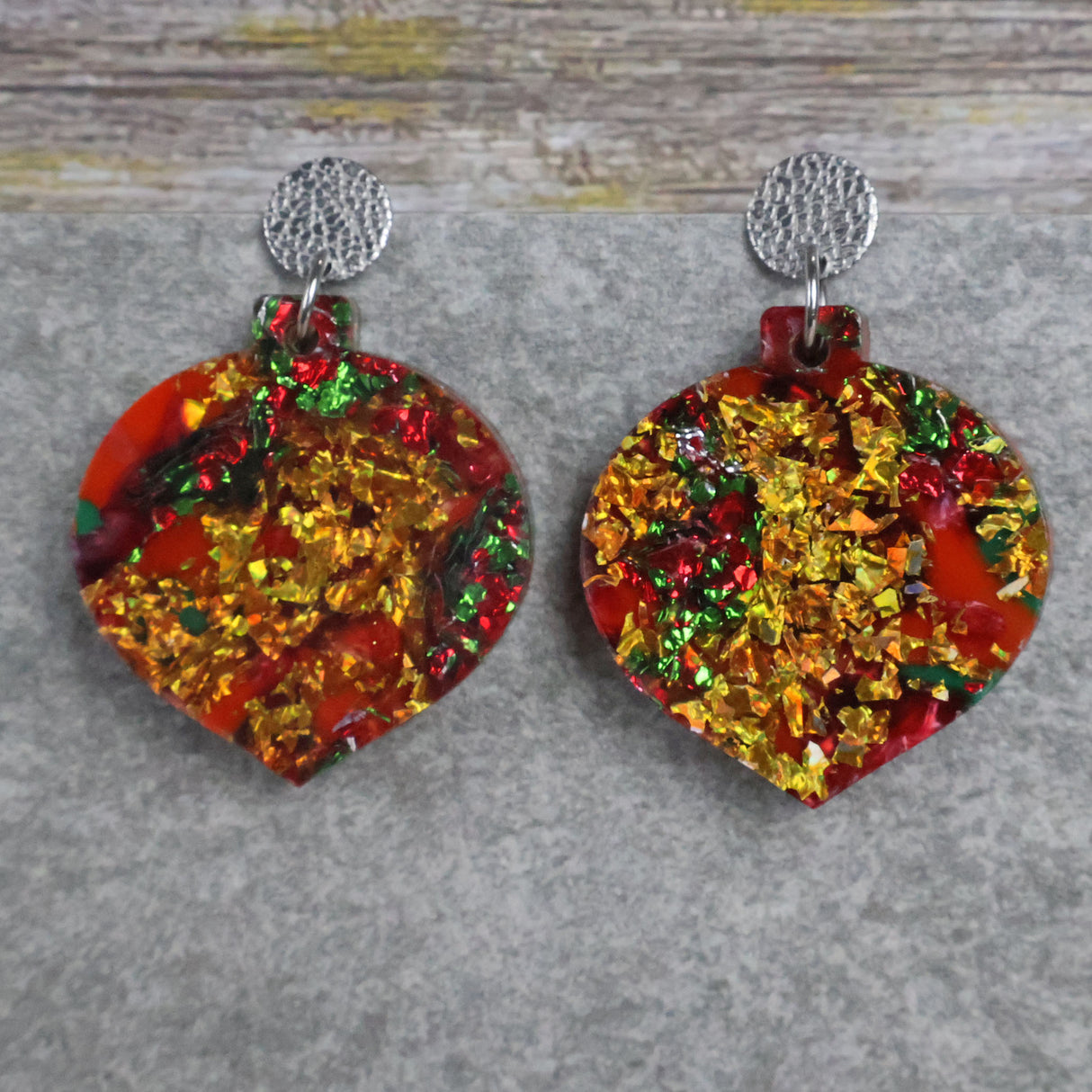 A pair of one of a kind recycled acrylic Christmas bauble earrings with stainless steel toppers, featuring a red, green and gold acrylic design. Pair 107-07