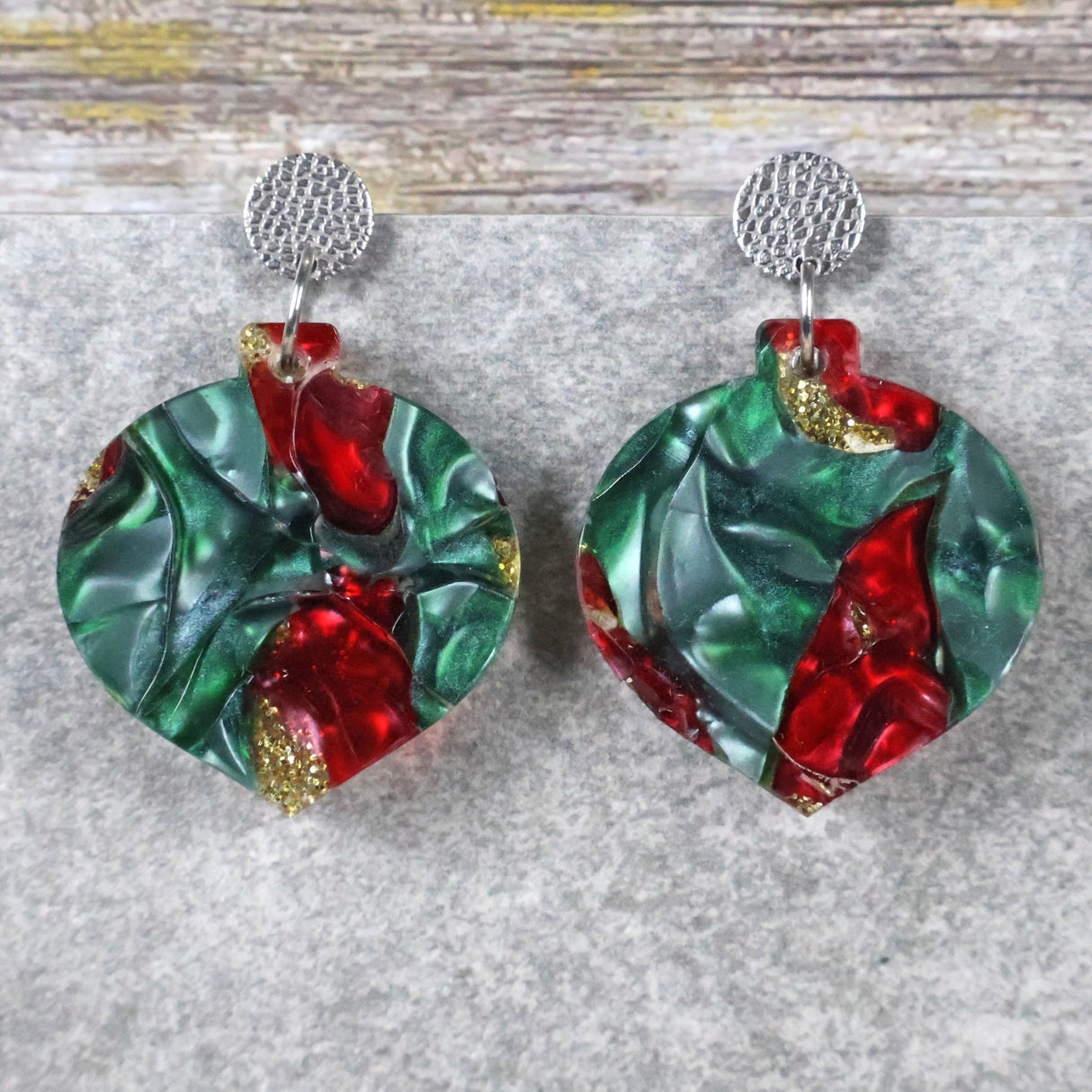 A pair of one of a kind recycled acrylic Christmas bauble earrings with stainless steel toppers, featuring a red, green and gold acrylic design. Pair 108-05