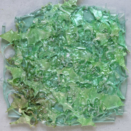 A melt pressed recycled acrylic sheet showing a randomised assortment of green coloured acrylic scraps pressed within.
