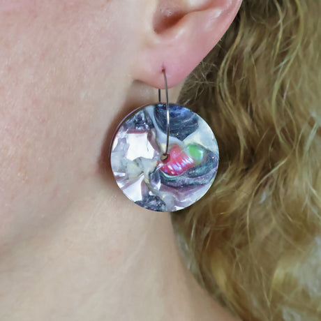 A pair of recycled acrylic disc earrings handing from stainless steel hoops, being modelled on an ear