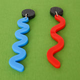 Pair of asymmetrical acrylic earrings with blue and red wavelength designs on a green background, angled view