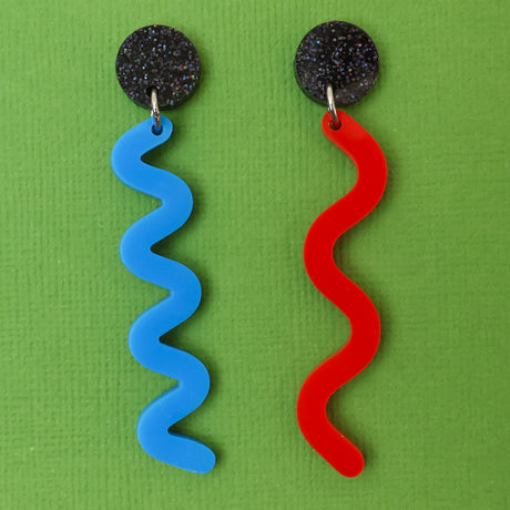 Pair of asymmetrical acrylic earrings with blue and red wavelength designs on a green background