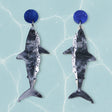 Closeup view of acrylic salmon shark shaped earrings with blue circular earring toppers