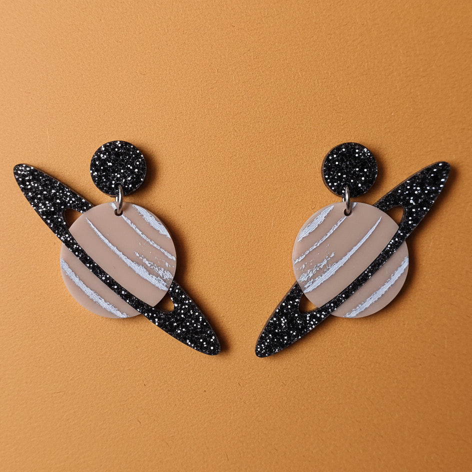 Pair of earrings with a saturn planet design, including black glittery rings. 