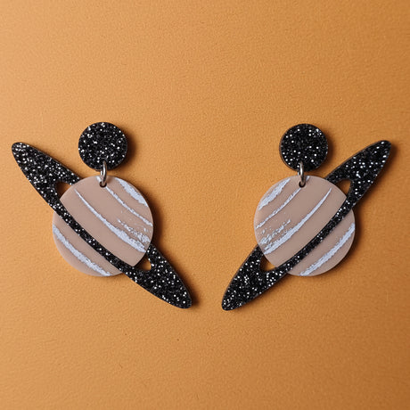 Pair of earrings with a saturn planet design, including black glittery rings. 
