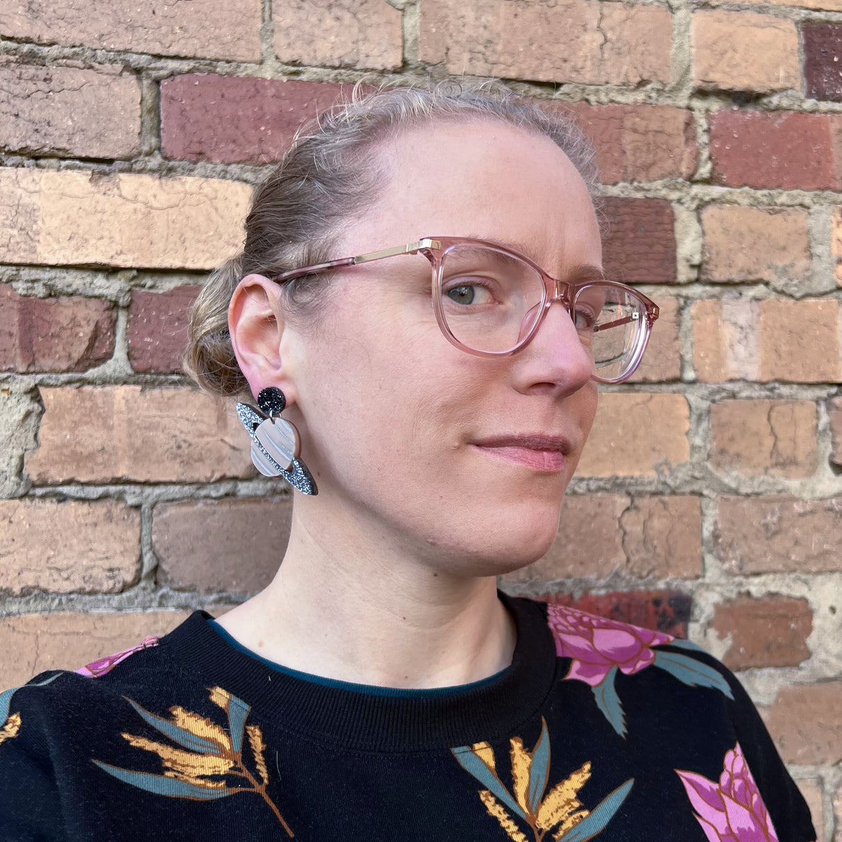 Acrylic Saturn earrings being modelled by the maker, a woman with blonde hair and glasses.