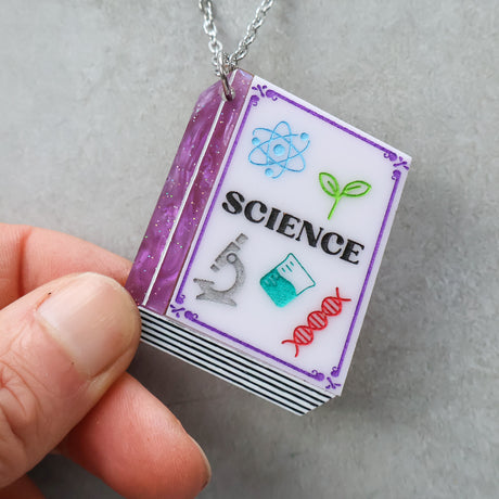 Necklace with a pendant shaped like a textbook titled 'Science' held by a hand in purple tones