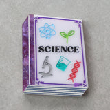Small purple toned book brooch with 'SCIENCE' and related icons 