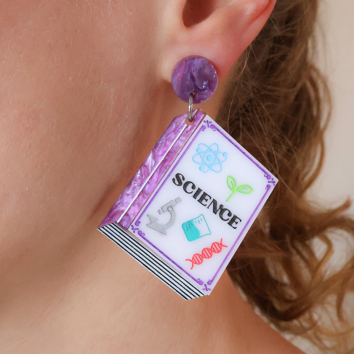 Purple toned Textbook shaped earrings with 'SCIENCE' title worn by a person