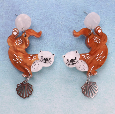 A pair of acrylic earrings with sea otter design on a light blue background