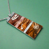 A pendant representing sedimentary layers, rectangular in shape and comprising 6 strips of different grey and brown acrylics, with a t-rex skull, fish bones and nautilus engraved and handpainted in the larger layers. The pendant hangs on a fine stainless steel chain.