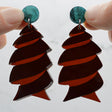 Closeup of dark brown acrylic cork screw shark egg earrings with green toppers being held up to show the transparency in the brown acrylic. 