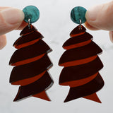 Closeup of dark brown acrylic cork screw shark egg earrings with green toppers being held up to show the transparency in the brown acrylic. 