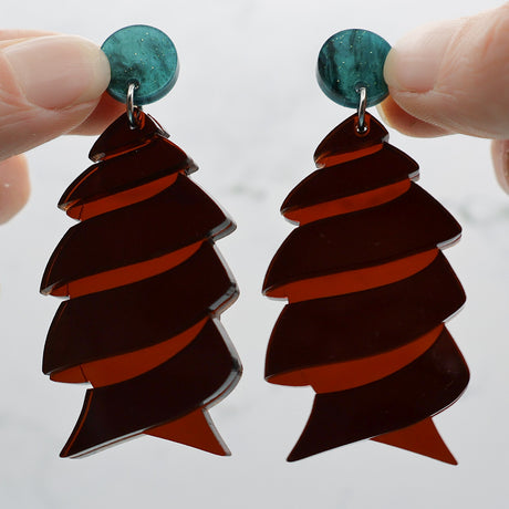 Closeup of dark brown acrylic cork screw shark egg earrings with green toppers being held up to show the transparency in the brown acrylic. 