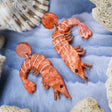 Laser cut acrylic orange shrimp earrings, closeup.