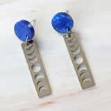 A pair of earrings with blue acrylic round toppers and rectangular stainless steel moon phase dangles.
