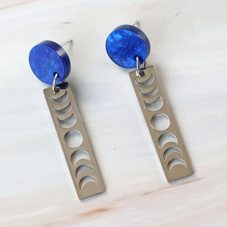 A pair of earrings with blue acrylic round toppers and rectangular stainless steel moon phase dangles.