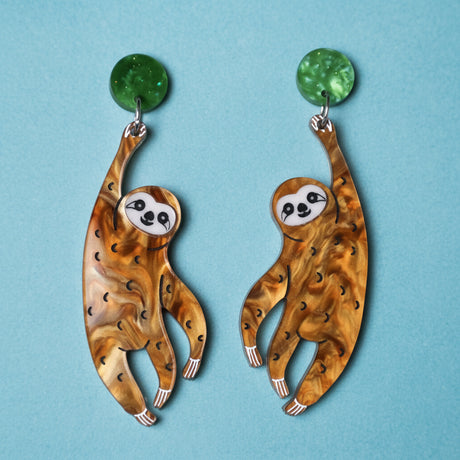 Closeup view of acrylic sloth earrings. Brown sloths hang from green acrylic earring toppers. 