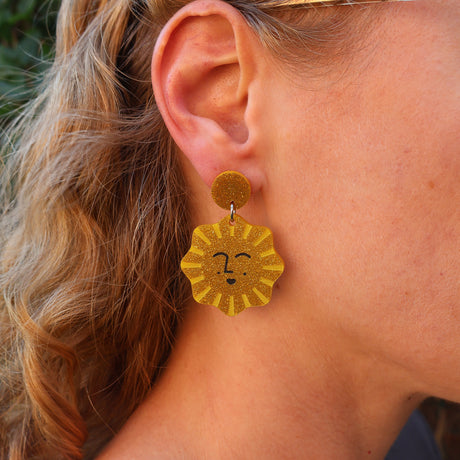 Close-up of a person wearing a gold sun-shaped earring with a smiling face design.