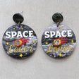 Earrings with 'Space Lover' design on a gray background with a meteor