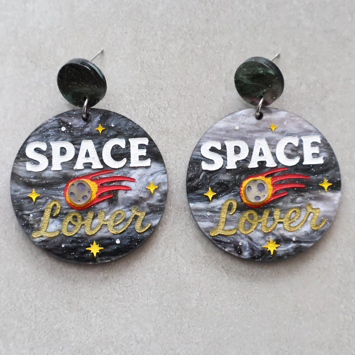 Earrings with 'Space Lover' design on a gray background with a meteor