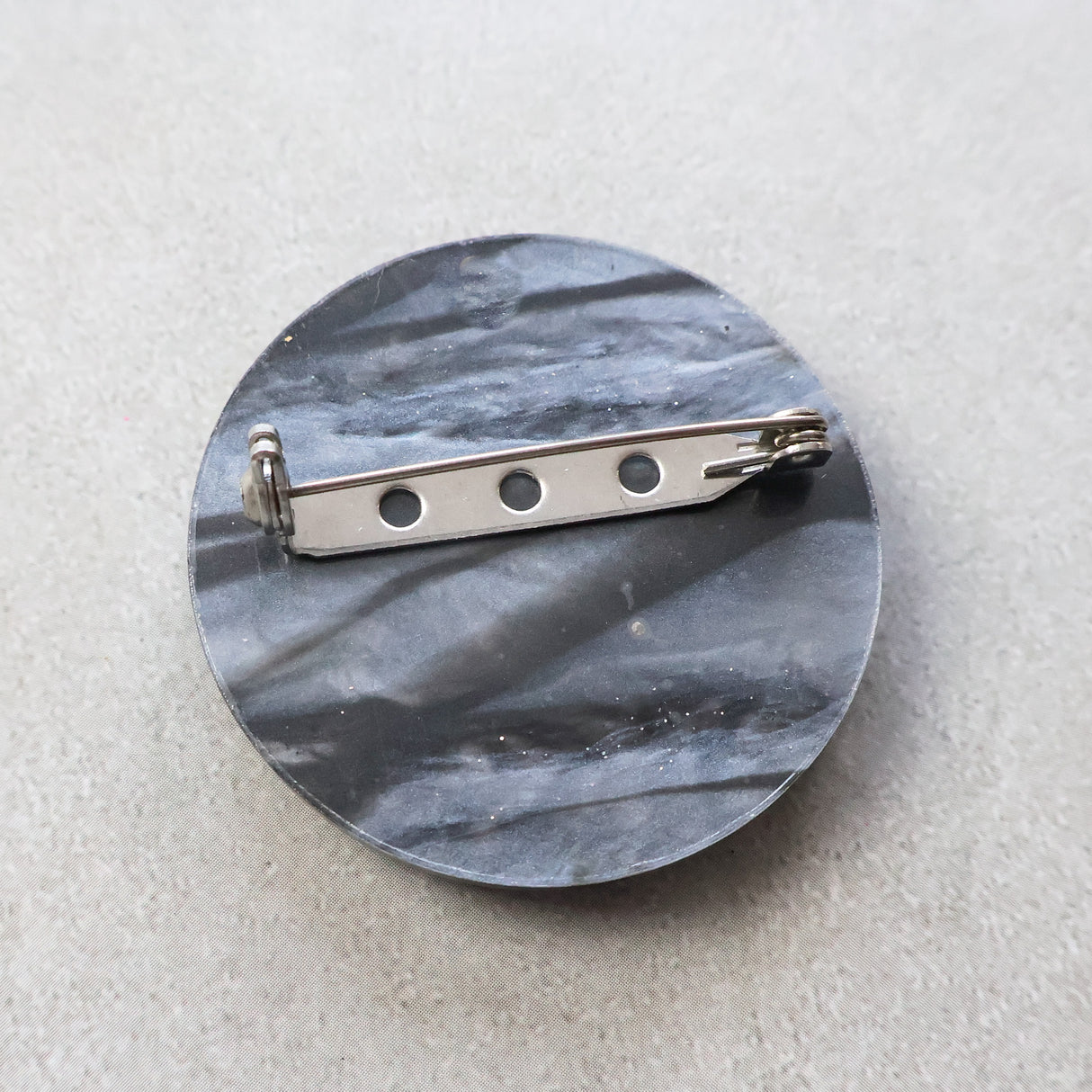 Round acrylicbrooch with a metal brooch pin on a light gray background