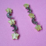 A pair of star and moon acrylic dangle earrings photographed at an angle. The earrings consist of alternating small yellow moon and grey/brown stars. 