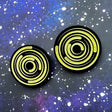 A pair of round acrylic star trail studs, black with gold painted star trails within. 