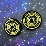 A pair of round acrylic star trail studs, black with gold painted star trails within. 
