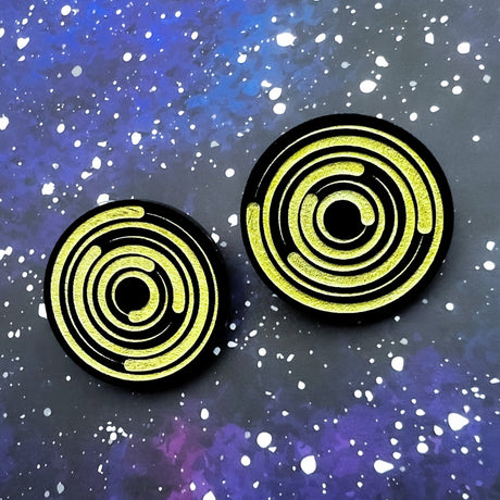 A pair of round acrylic star trail studs, black with gold painted star trails within. 