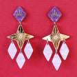 Gold pink and purple statement dangle earrings with a star focal piece against a deep red backdrop. Front View