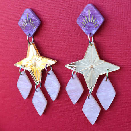 Gold pink and purple statement dangle earrings with a star focal piece against a deep red backdrop. Side angled view
