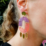 Close-up of a person wearing statement oval shaped purple pink and gold dangle earrings